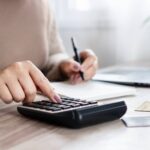 Pessoa usando calculadora e anotações.